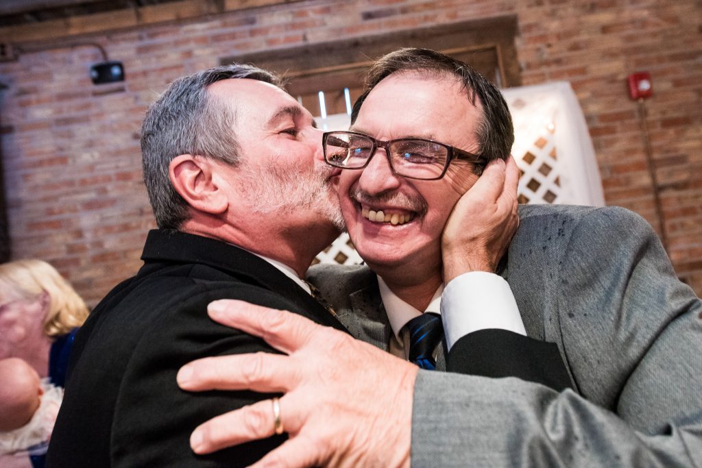 Man kissing another man on cheek joyously