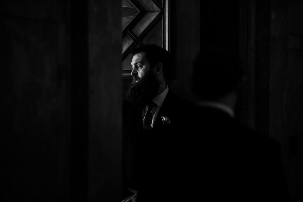 wedding photo black and white of bearded man illuminated by a narrow door.