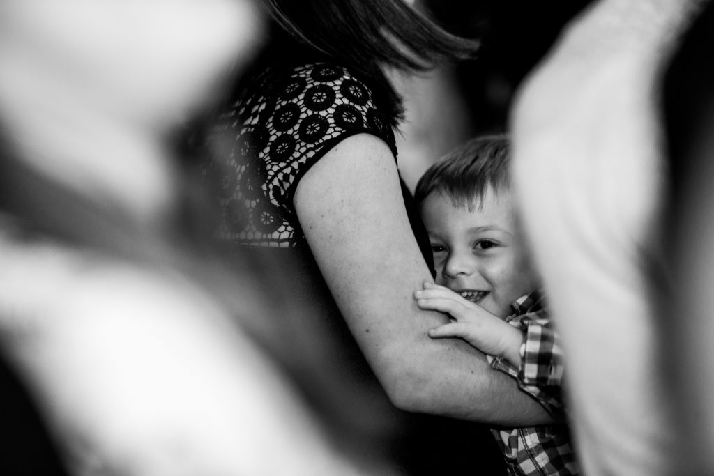 child in black and white smiles from his mothers arms who is out of frame